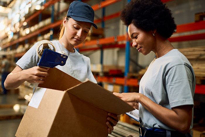 Two women in warehouse check contents of a box.