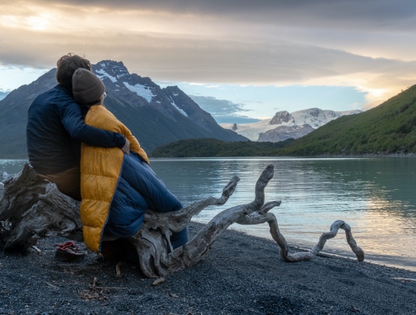 Couple site on log by serene mountain lake.