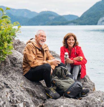 Older couple take a water break on Alaskan hike.